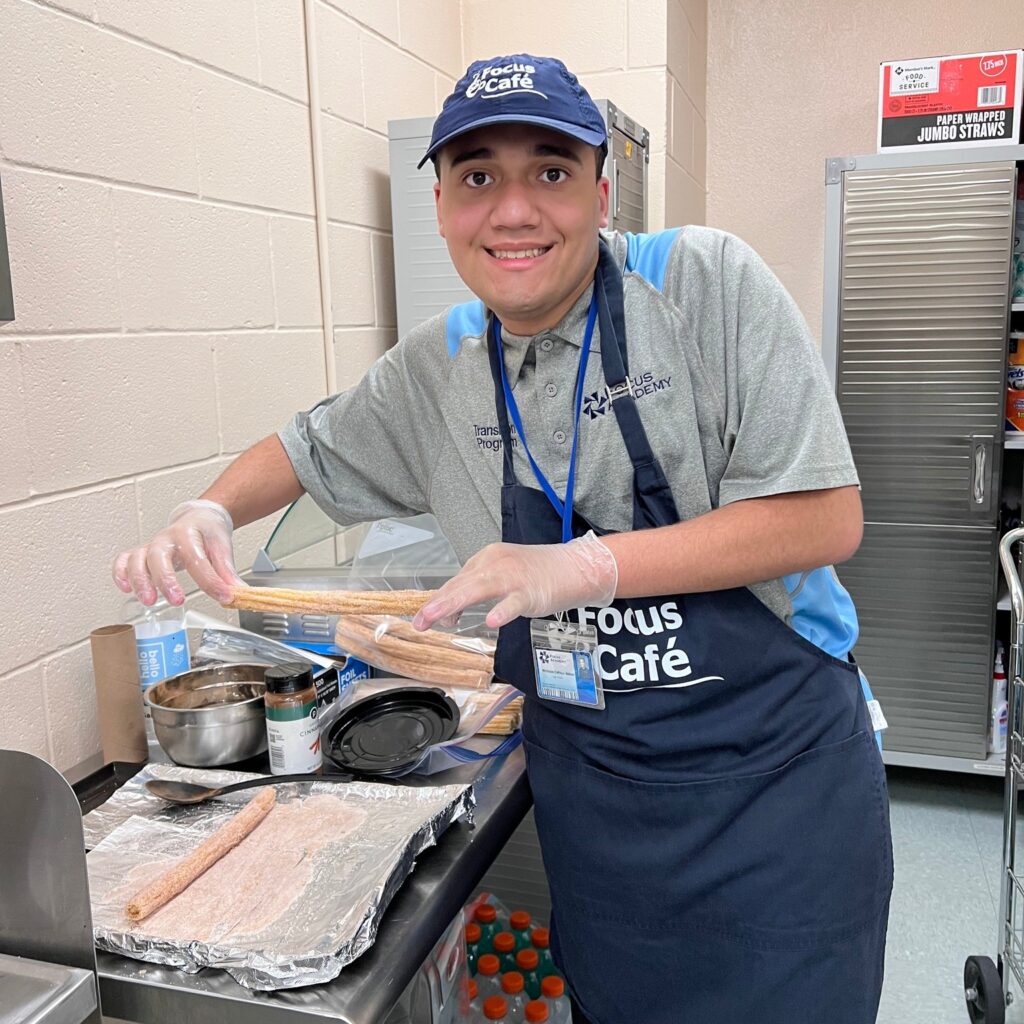 Focus Cafe team member wearing an apron and gloves preparing churros in a kitchen