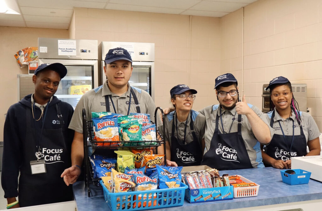 Five Focus Cafe team members standing behind a snack display counter in a kitchen area