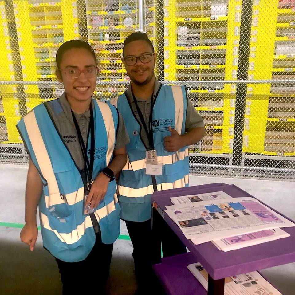 Two Focus employment training program participants wearing safety vests stand in a warehouse.